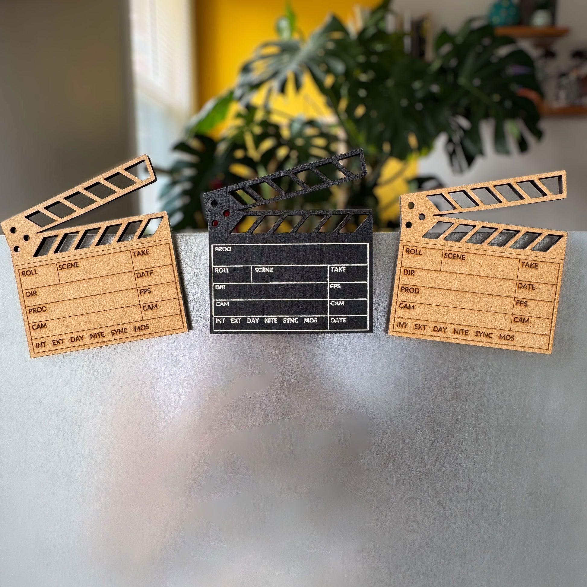 front view of three engraved wooden clapboard magnets in brown and black on a metal fridge in a studio room