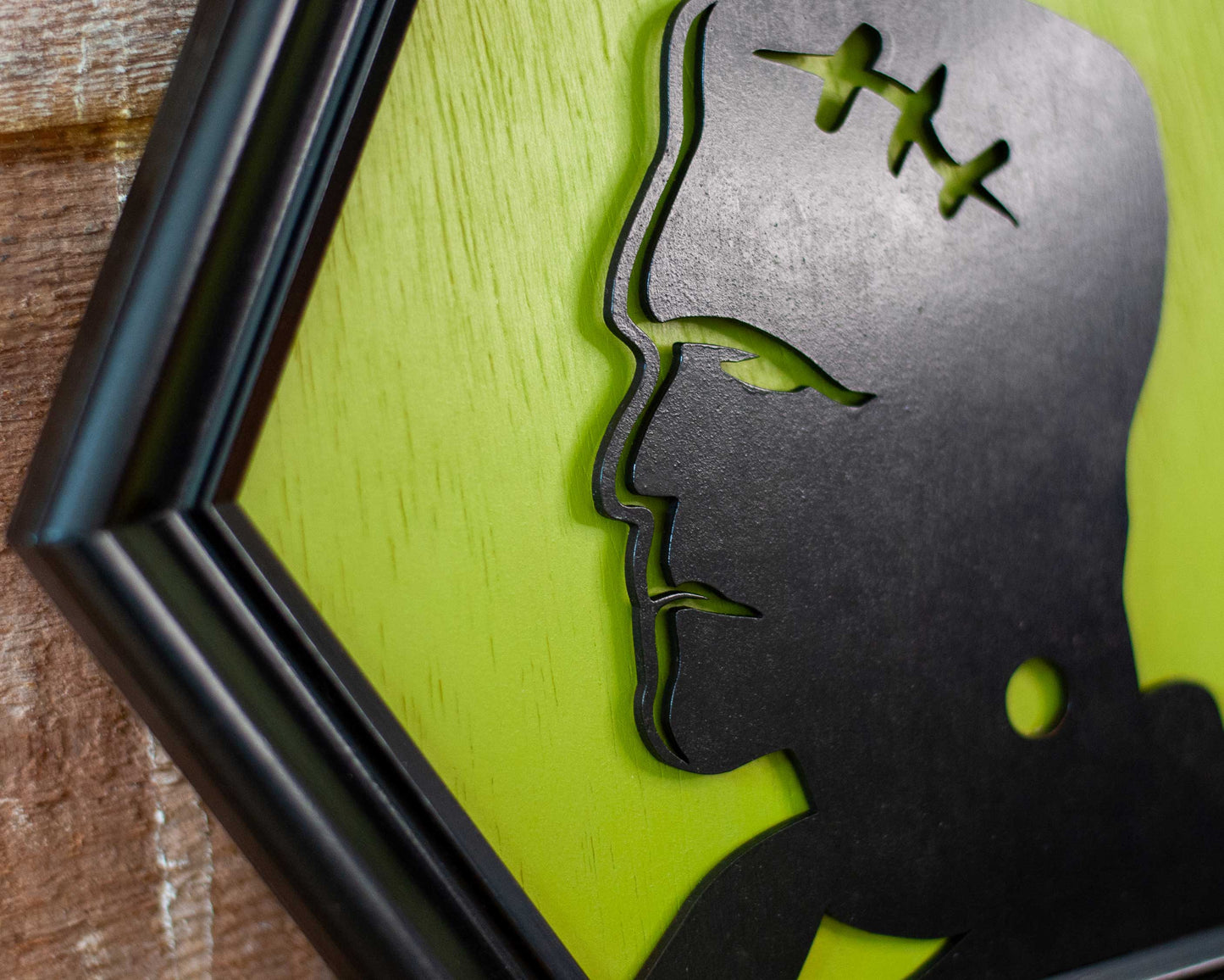 Hexagonal frame with a black silhouette of a modern Frankenstein on a green background against a brick wall.