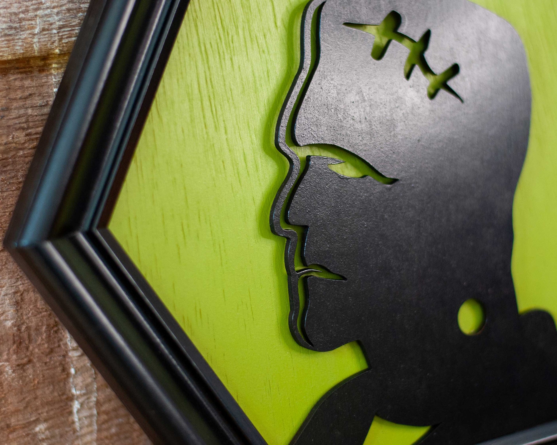 Hexagonal frame with a black silhouette of a modern Frankenstein on a green background against a brick wall.