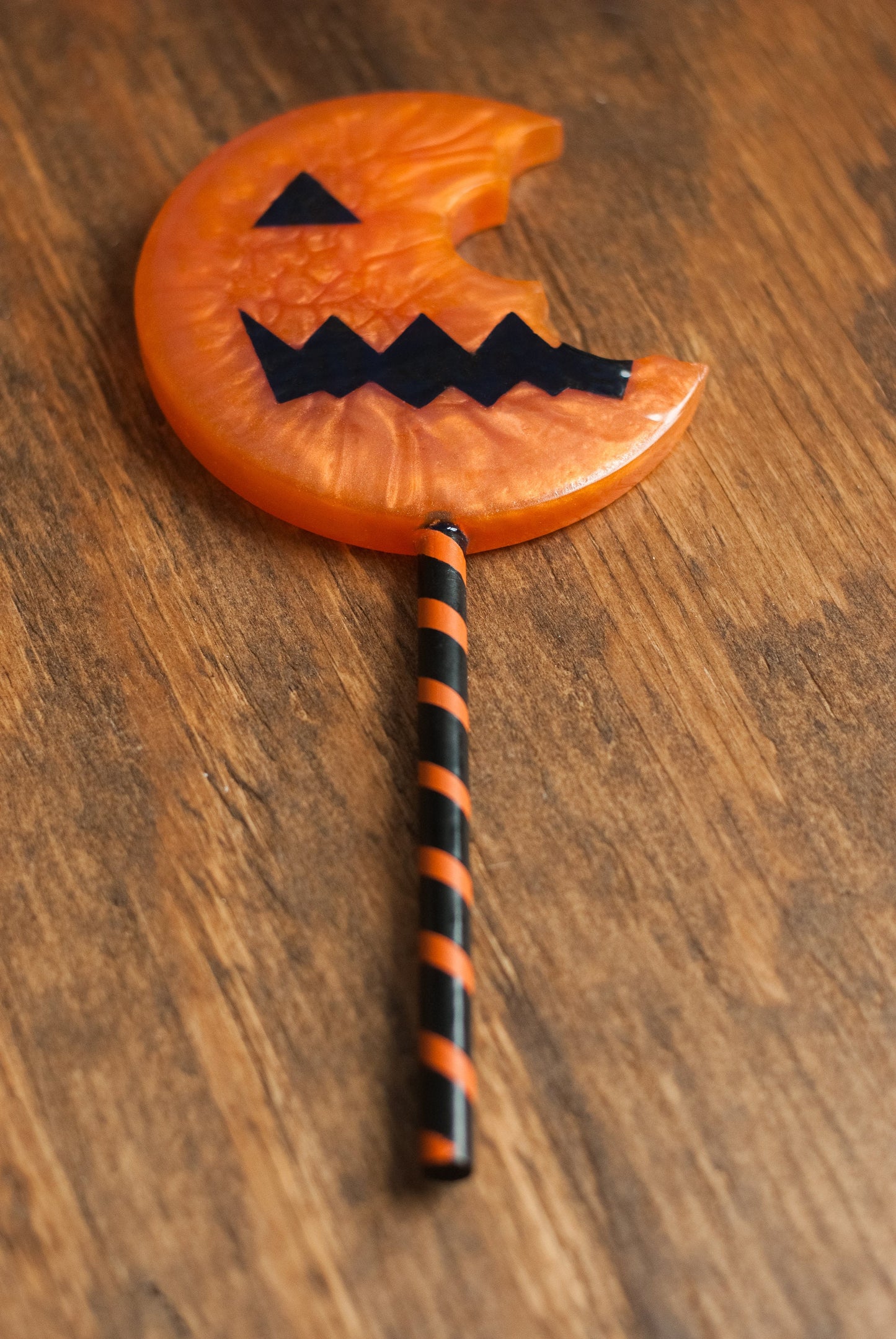 Top down view of black and orange Halloween-themed horror movie pumpkin lollipop prop made of resin for trick or treat and cosplay displayed on wooden table