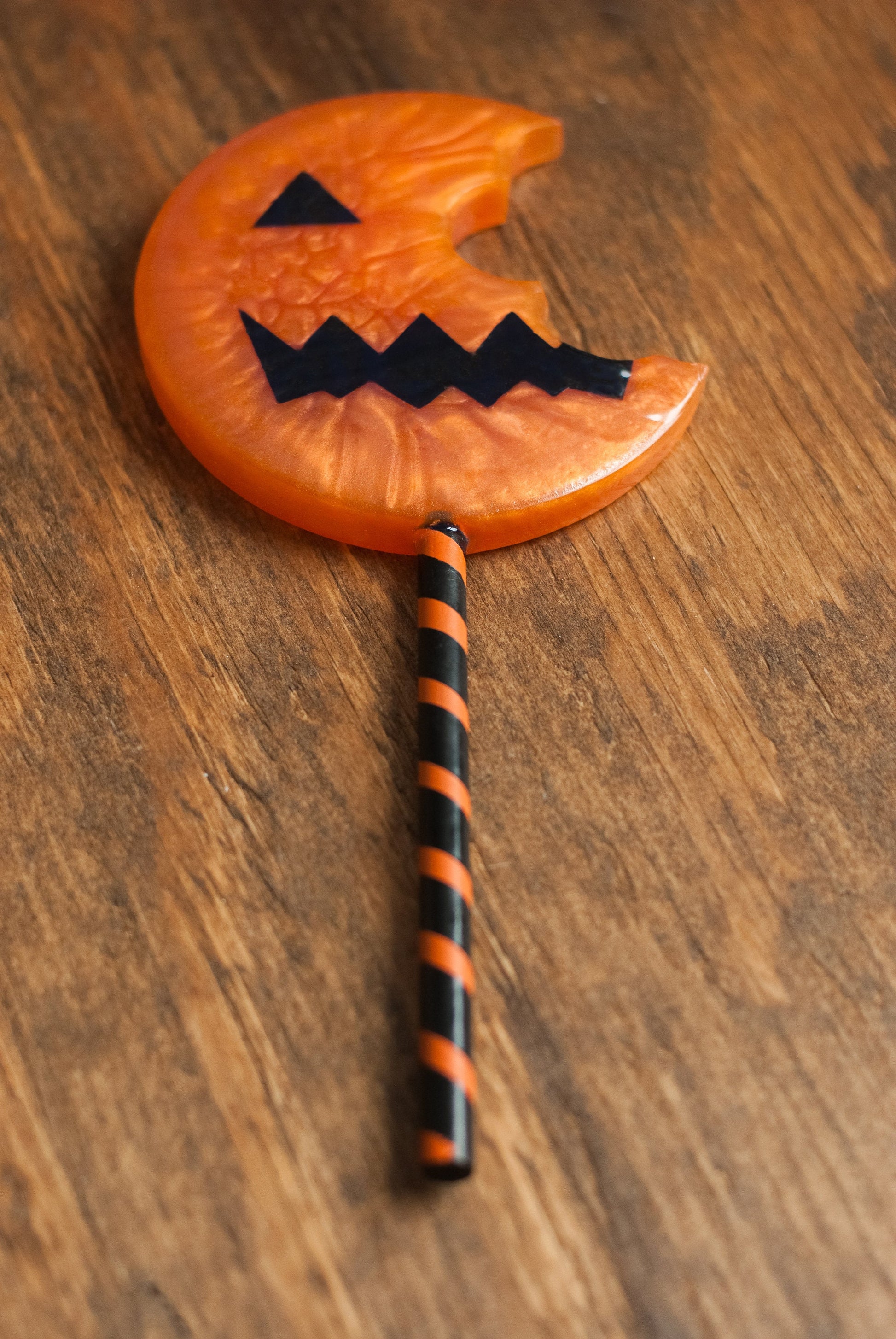 Top down view of black and orange Halloween-themed horror movie pumpkin lollipop prop made of resin for trick or treat and cosplay displayed on wooden table