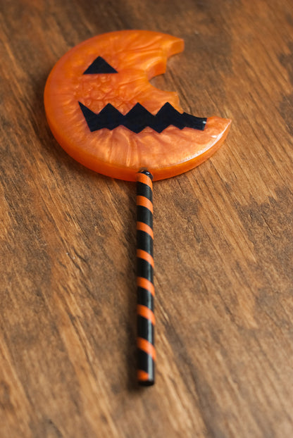 Top down view of black and orange Halloween-themed horror movie pumpkin lollipop prop made of resin for trick or treat and cosplay displayed on wooden table
