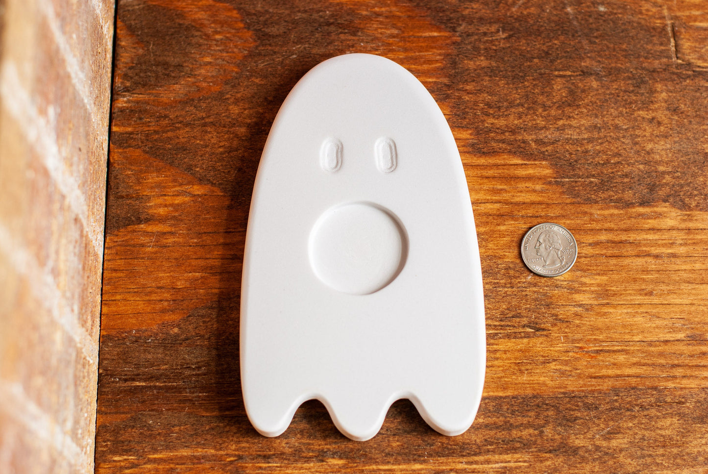 White ghost-shaped tea light holder on a wooden surface with a coin for scale