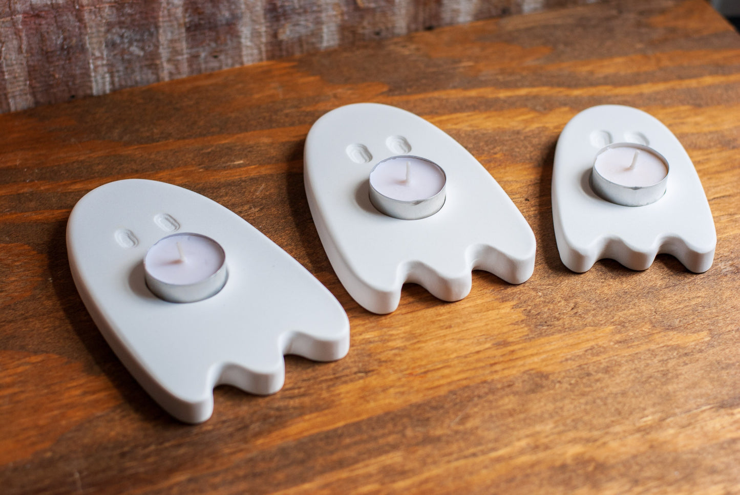 Three ghost-shaped candle holders with candles on a wooden surface