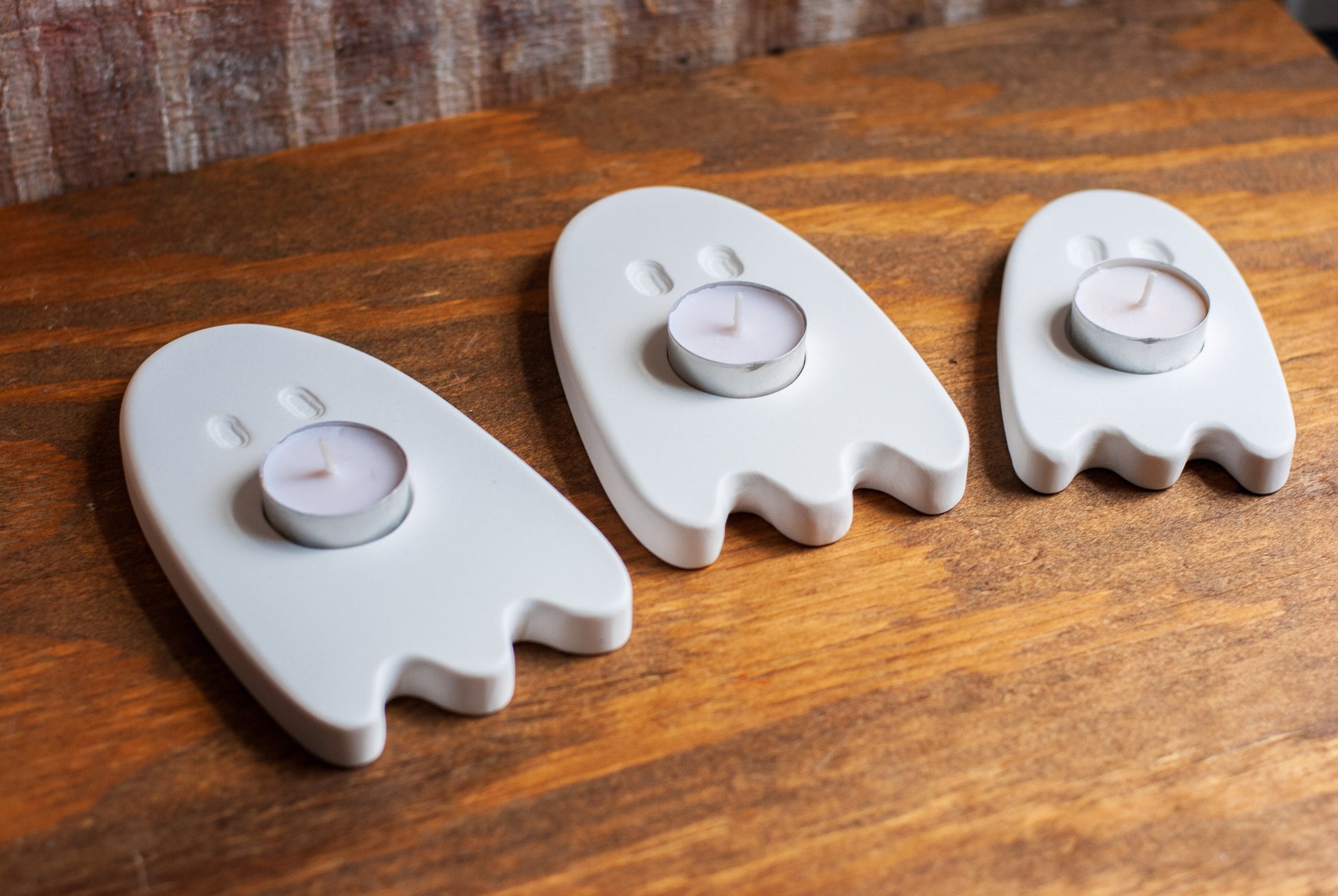Three ghost-shaped candle holders with candles on a wooden surface