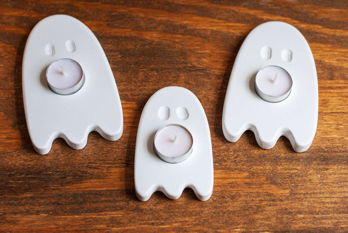 Three ghost-shaped candle holders with candles on a wooden surface