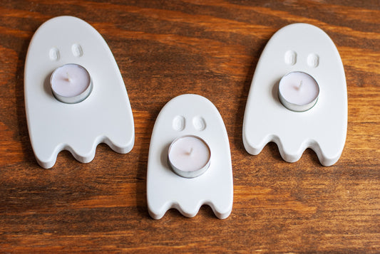 Three ghost-shaped candle holders with candles on a wooden surface