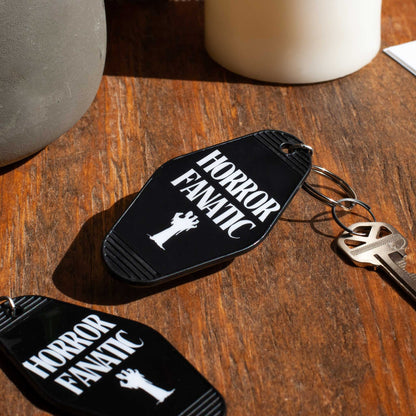 Black motel keychain with 'Horror Fanatic' text on a wooden surface