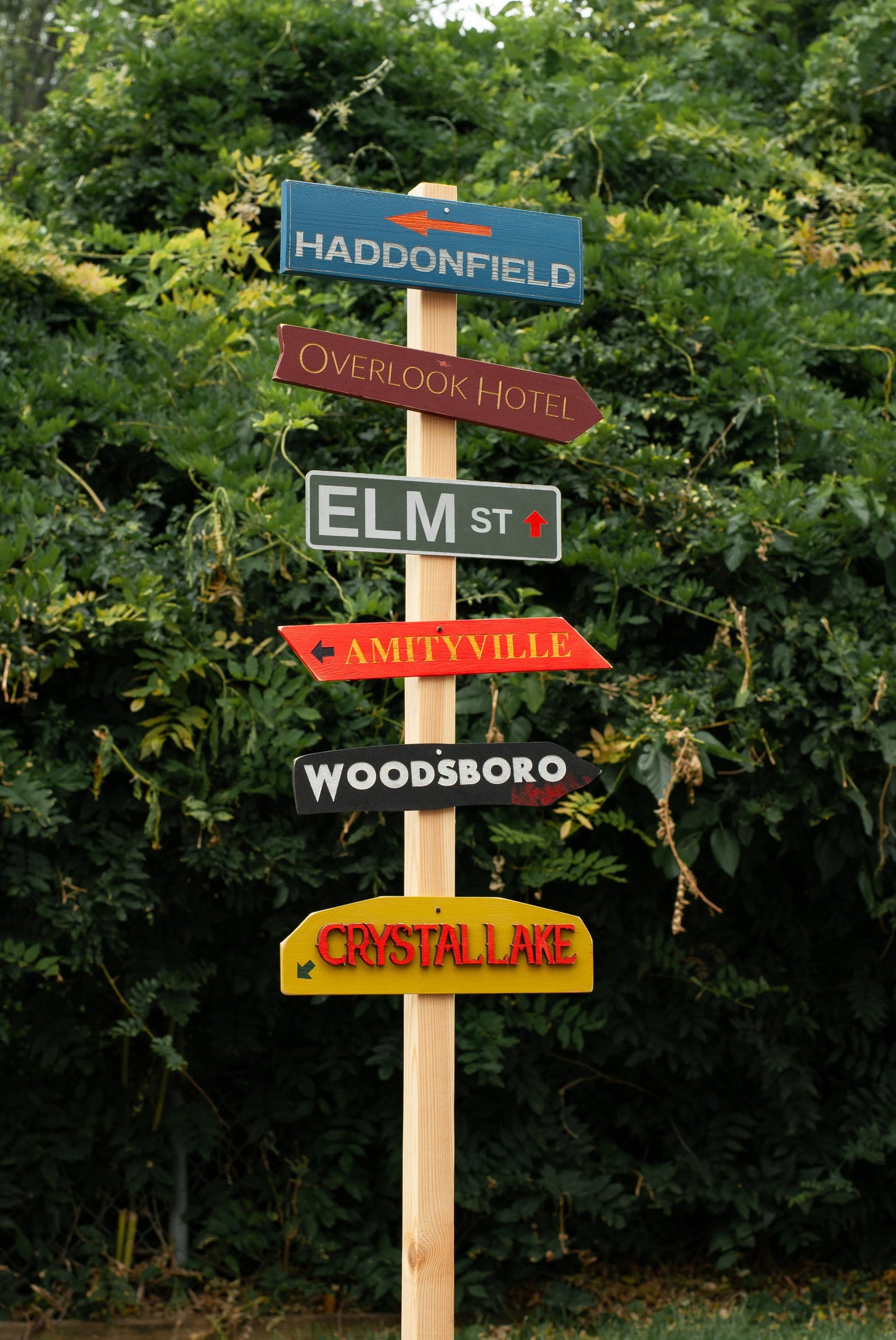 Wooden Horror Directional street and city signpost with various small scary movie signs on a green leafy background