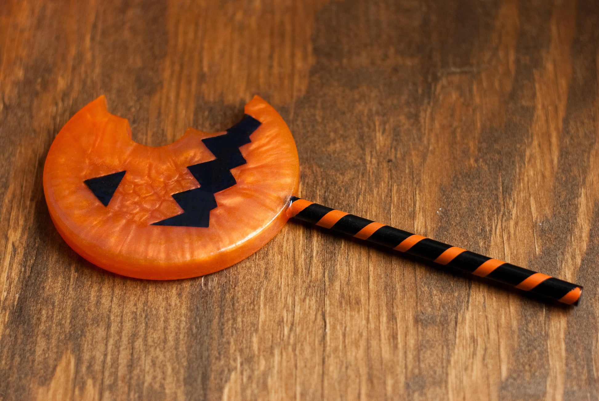Side view of black and orange Halloween-themed horror movie pumpkin lollipop prop made of resin for trick or treat and cosplay displayed on wooden table