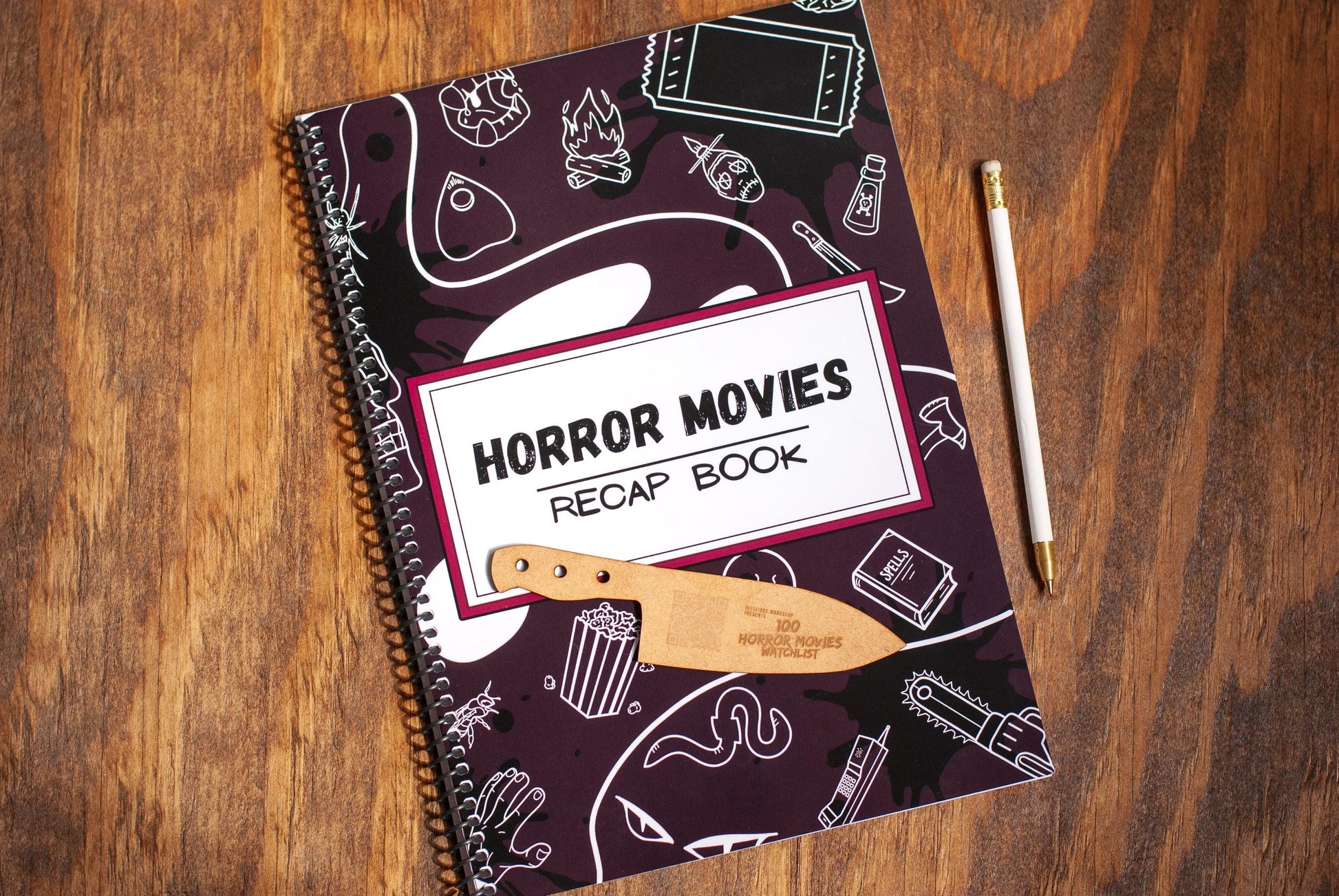 top view of horror movie review journal titled Horror Movies Recap book a spiral notebook on a wooden table with wood bookmark and pen