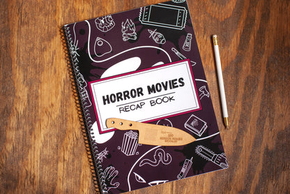 top view of horror movie review journal titled Horror Movies Recap book a spiral notebook on a wooden table with wood bookmark and pen