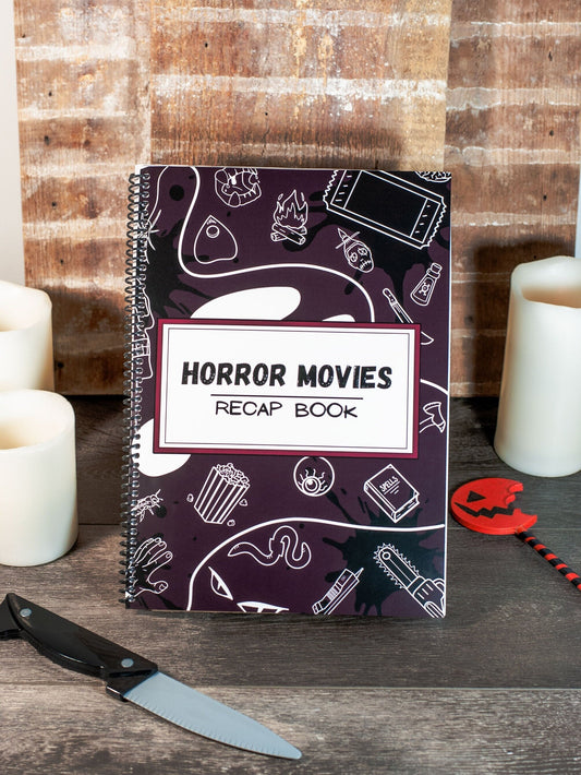 front view of a horror movie review journal with detailed front cover design on a table with spooky candles and halloween decor