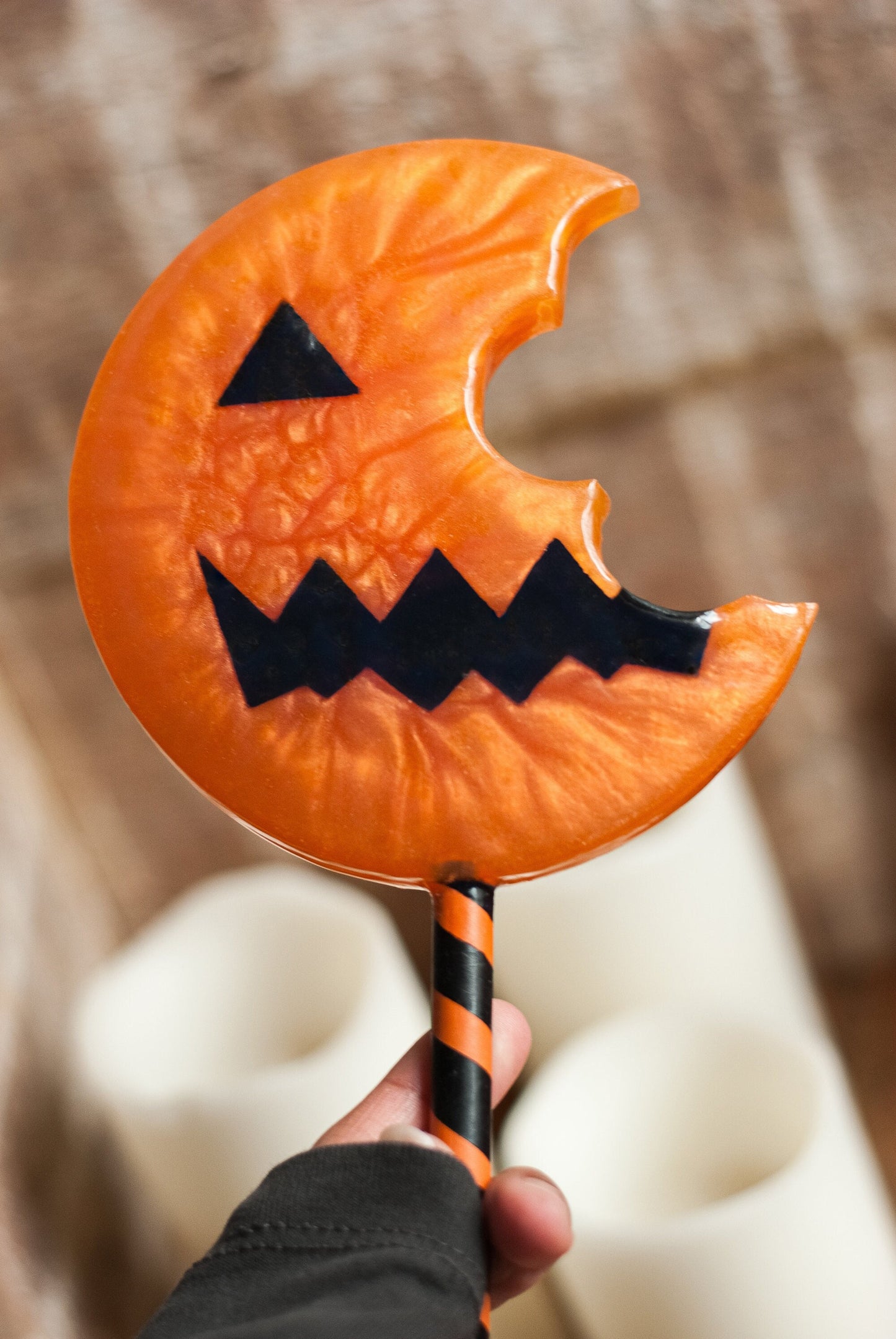 Hand holding a Halloween-themed candy shaped jack-o'-lantern lollipop prop 