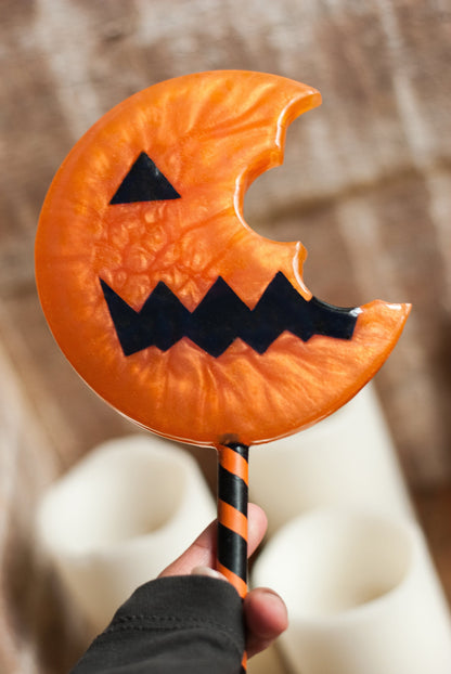 Hand holding a Halloween-themed candy shaped jack-o'-lantern lollipop prop 