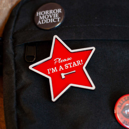 Red star-shaped pin with 'Please I'm a Star!' text on a cross-body bag with other horror pins