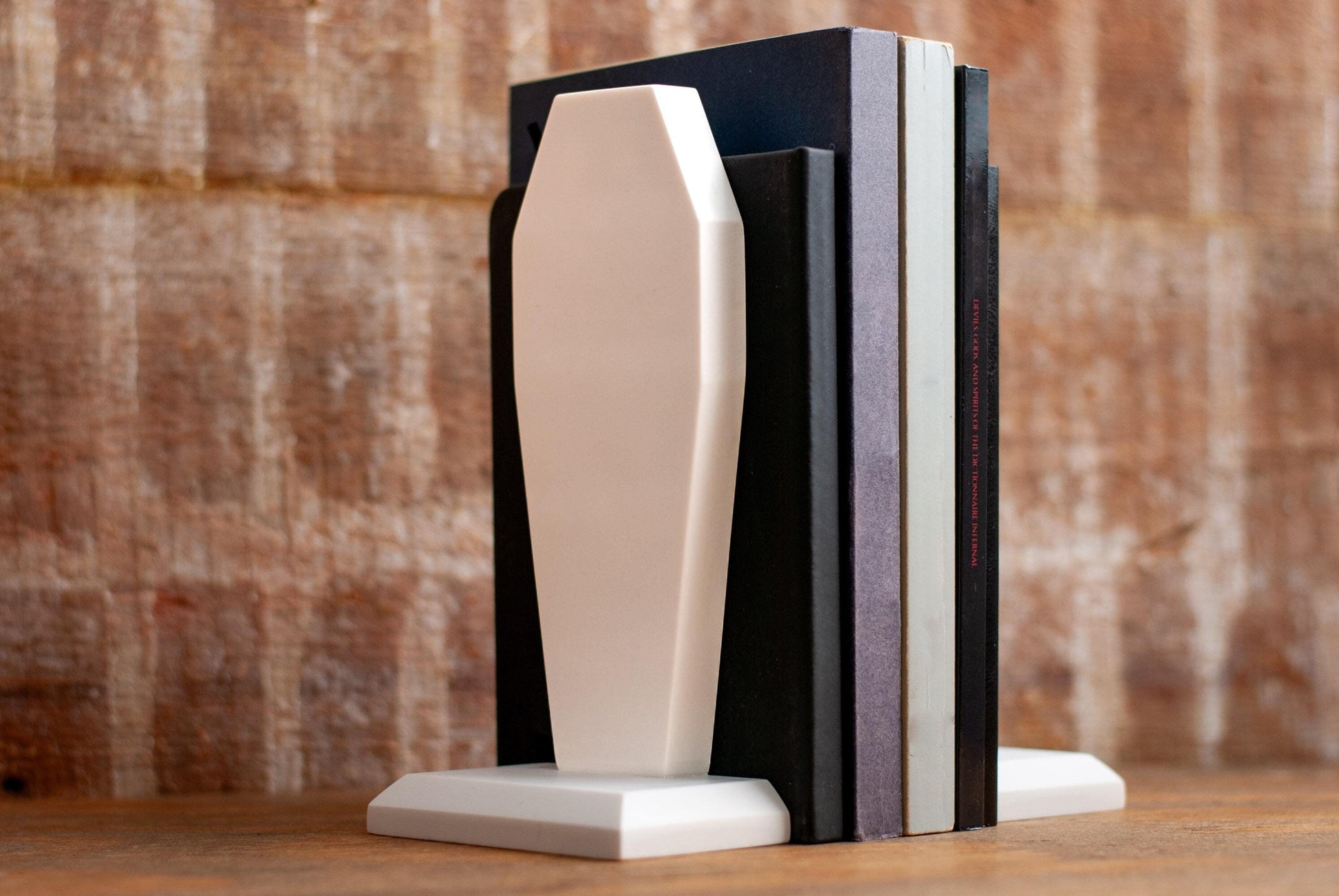Decorative coffin-shaped bookends made of white marble on a wooden table with a textured wood background