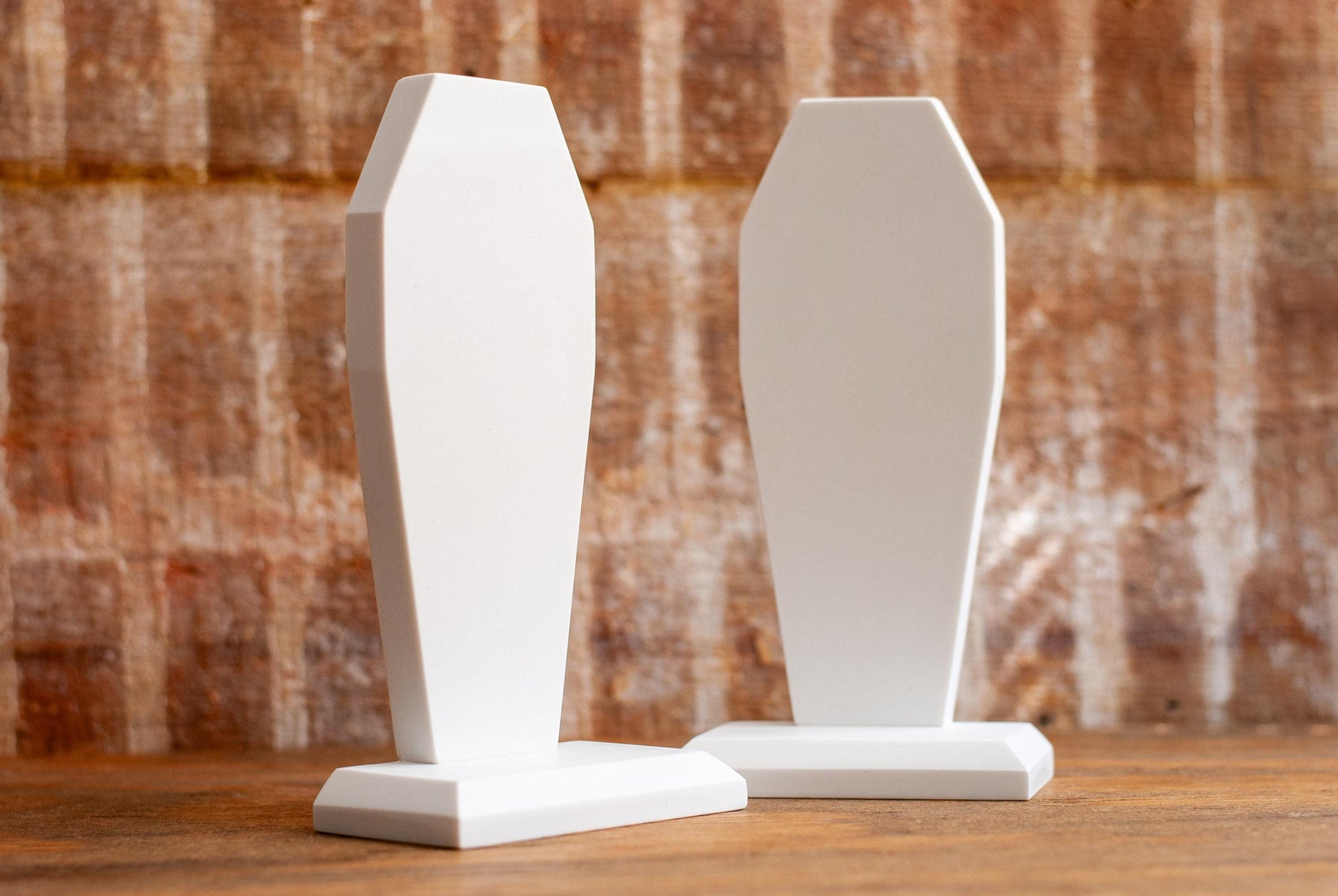 Two decorative coffin-shaped bookends made of white marble on a wooden table with a textured wood background