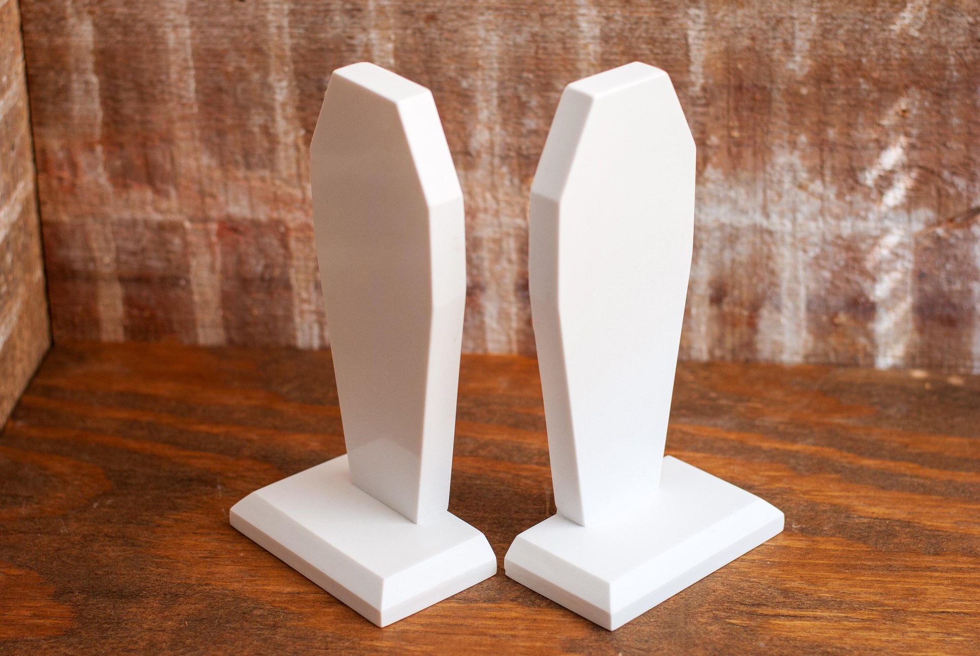 Two white marble coffin-shaped bookends on a wooden surface with a rustic background