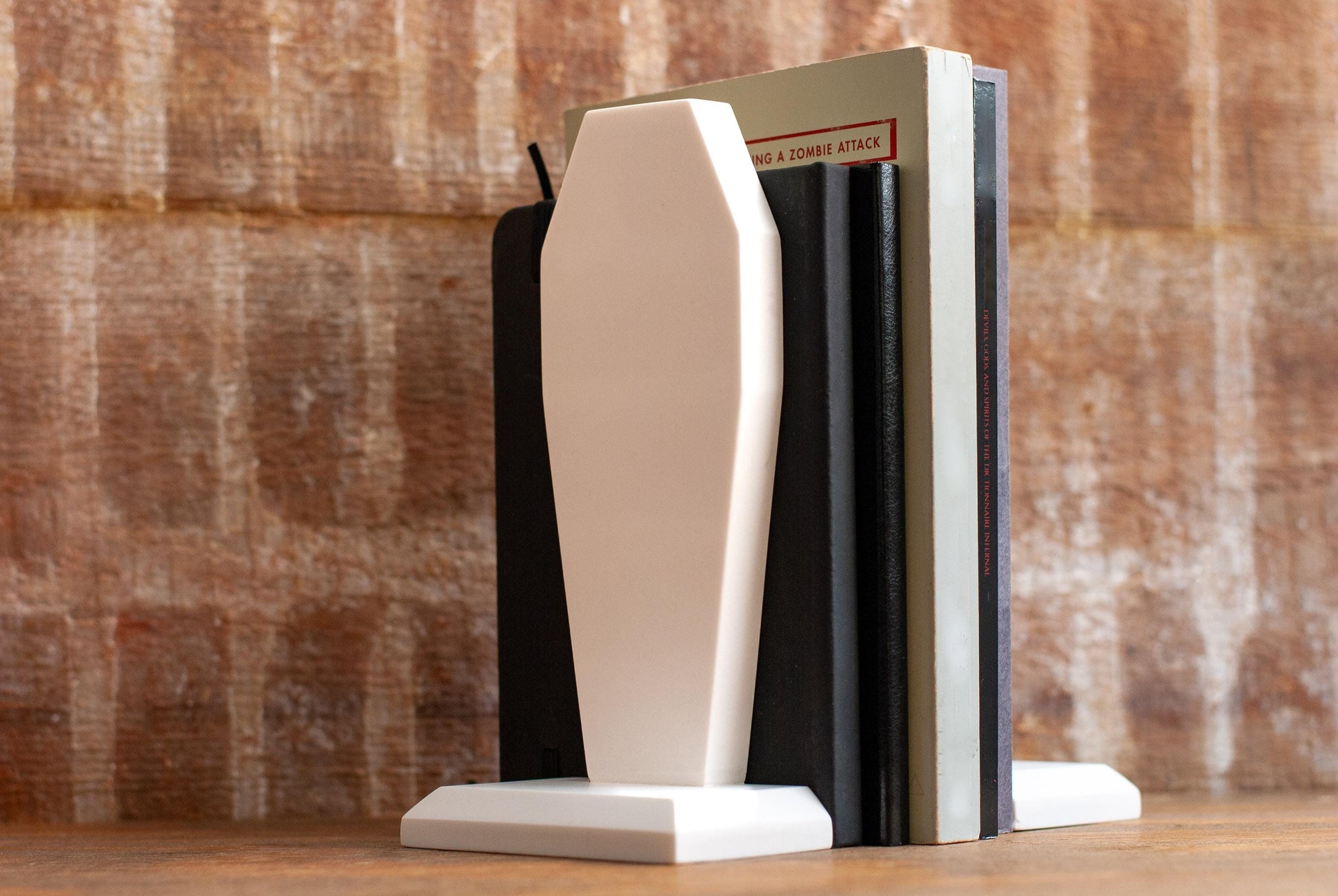 Decorative coffin-shaped bookends made of white marble with dark books between them on a wooden table with a textured wood background