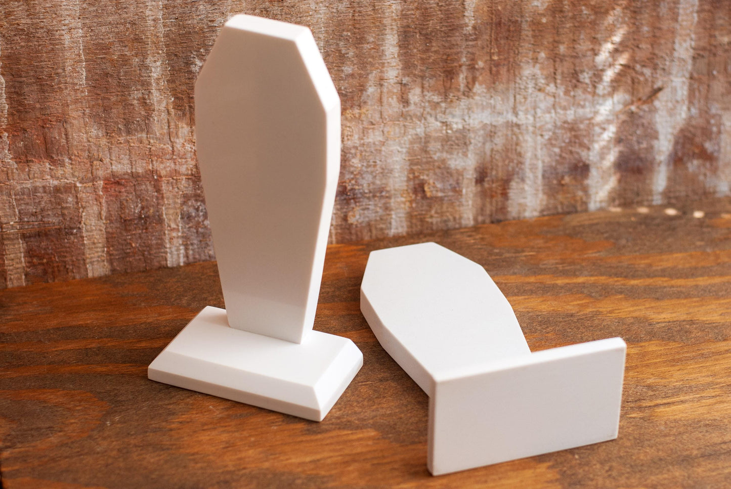 Two decorative coffin-shaped bookends made of white marble showing the bottom on a wooden table with a textured wood background