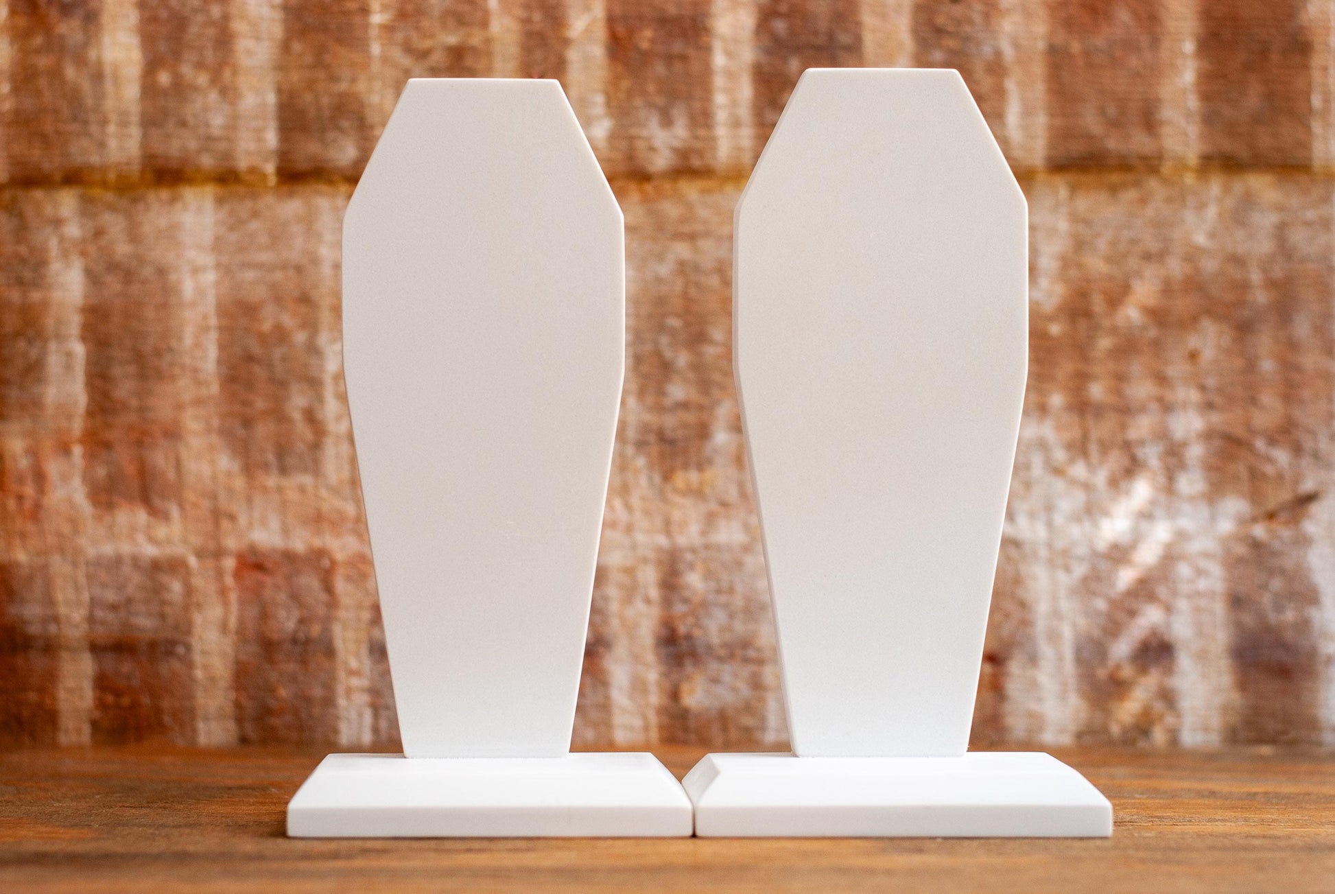 Two decorative coffin-shaped bookends made of white marble on a wooden table with a textured wood background