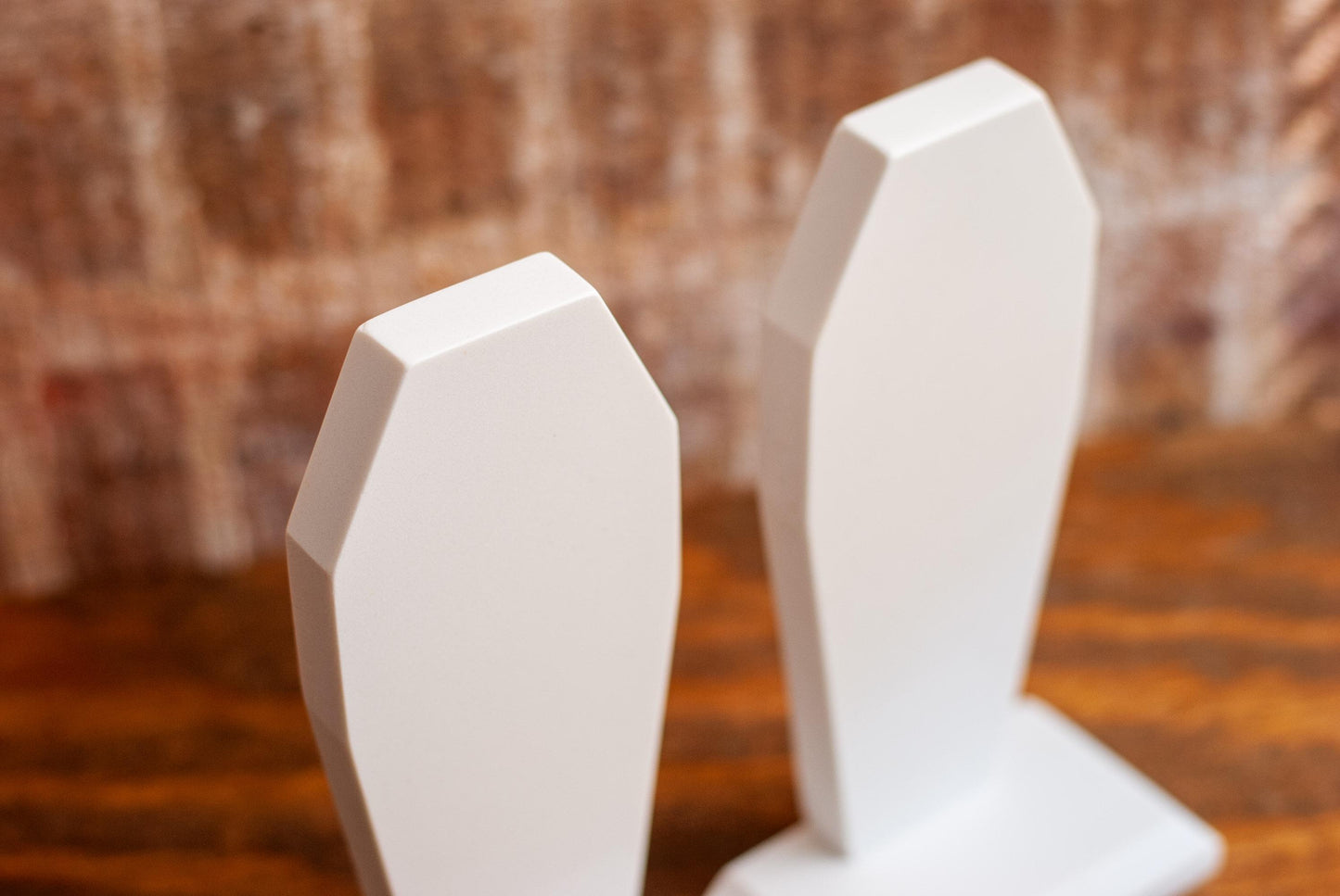 Close-up view of the top of two decorative coffin-shaped bookends made of white marble on a wooden table with a textured wood background