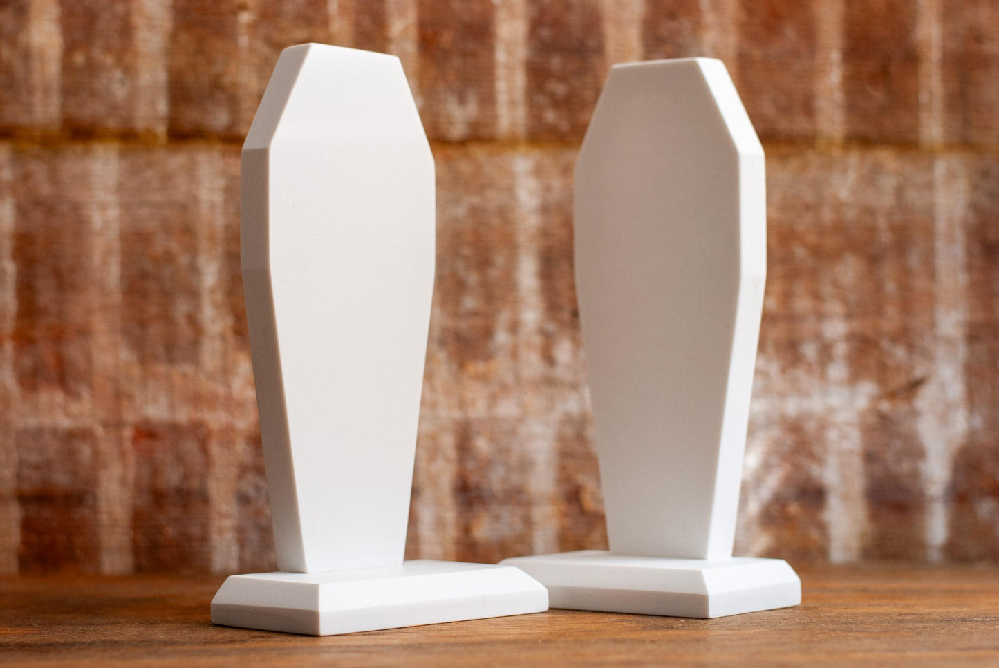 Two decorative coffin-shaped bookends made of white marble on a wooden table with a textured wood background