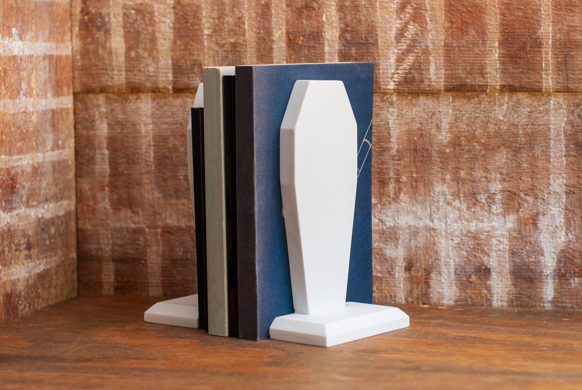 Two decorative coffin-shaped bookends made of white marble holding a set of books between them on a wooden table with a textured wood background