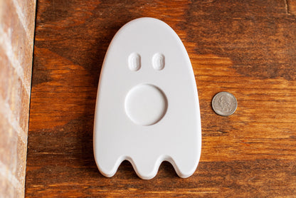 White ghost-shaped tea light holder on a wooden surface with a coin for scale
