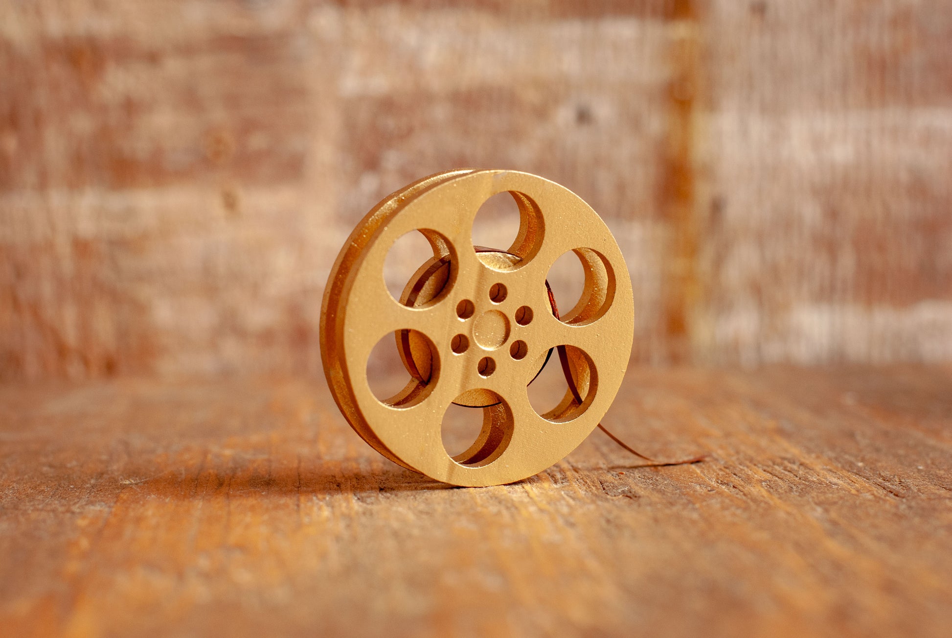 side view of a gold miniature movie reel magnet sitting on a wooden table