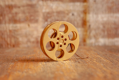 side view of a gold miniature movie reel magnet sitting on a wooden table