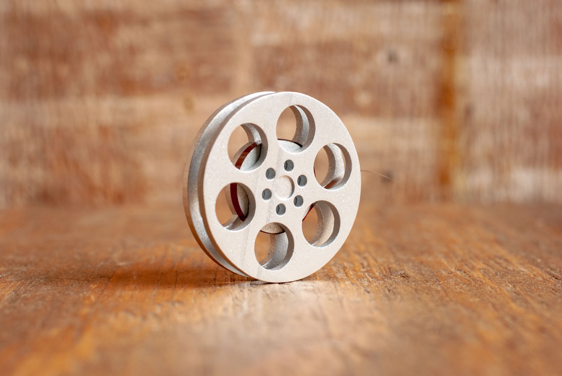 front view of a silver miniature movie reel magnet sitting on a wooden table