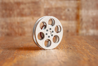 front view of a silver miniature movie reel magnet sitting on a wooden table