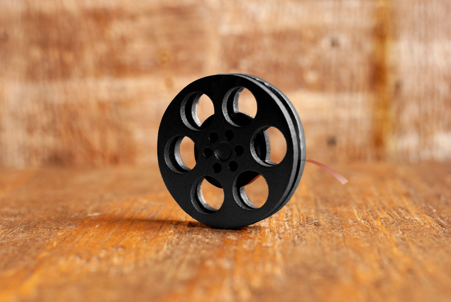 side view of a black miniature movie reel magnet sitting on a wooden table