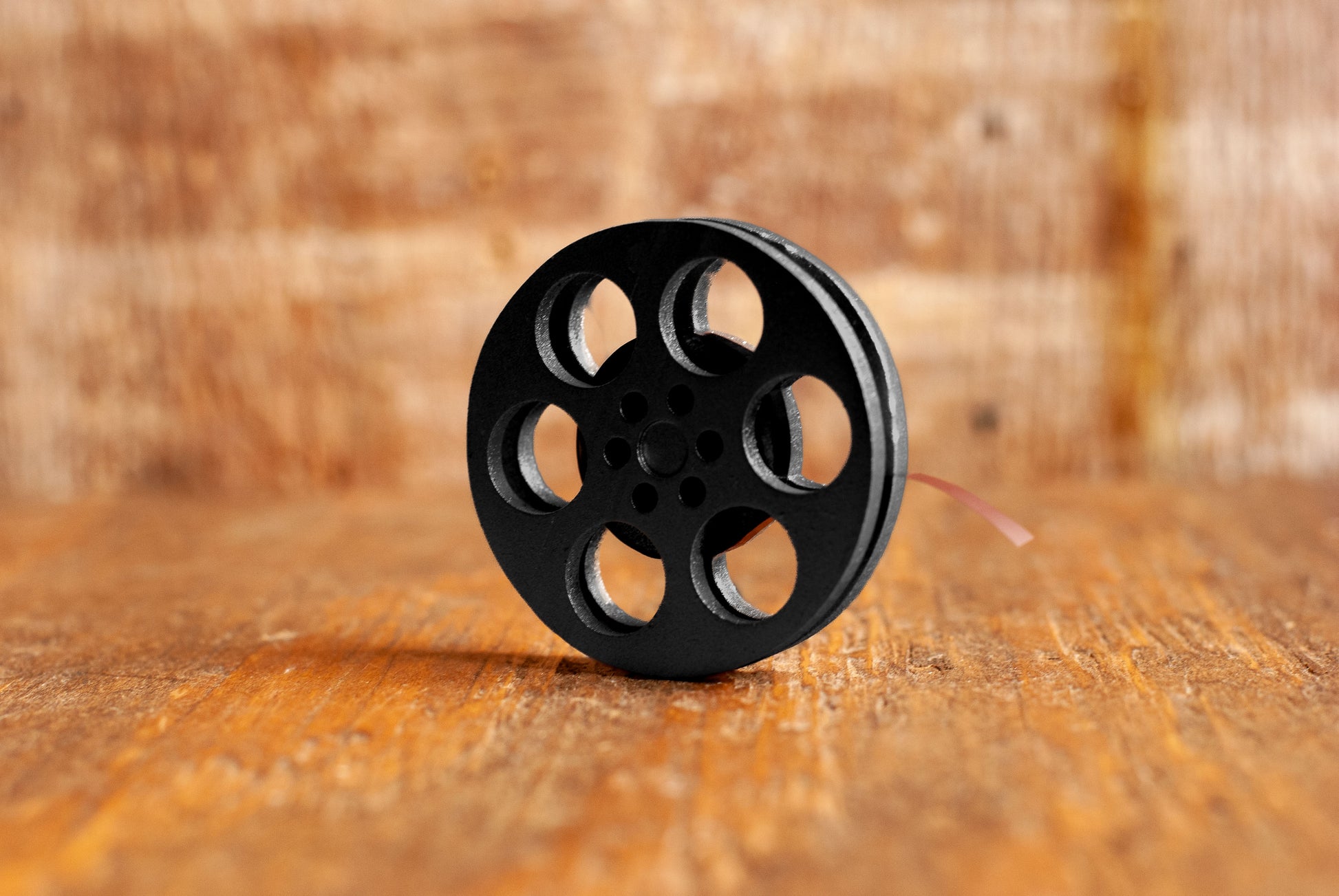 side view of a black miniature movie reel magnet sitting on a wooden table