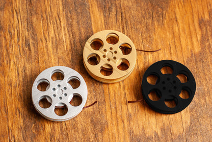 top view of a three miniature movie reel magnet in gold silver and black sitting on a wooden table