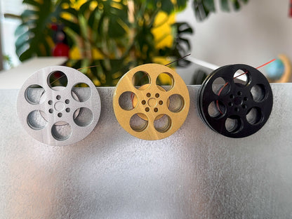 front view of three miniature movie reel magnets in gold silver and black holding up a refrigerator