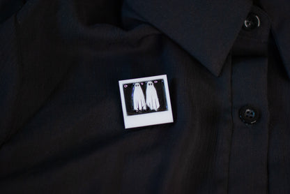 Black shirt with a white graphic pin featuring two ghosts in a white polaroid on a dark background