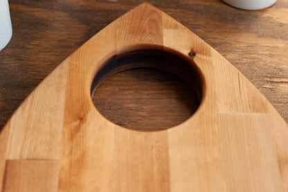 Wooden planchette-shaped cutting board with a central circular hole on a wooden surface