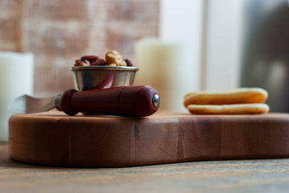 Wooden planchette-shaped cutting board with food on top and a blurred background
