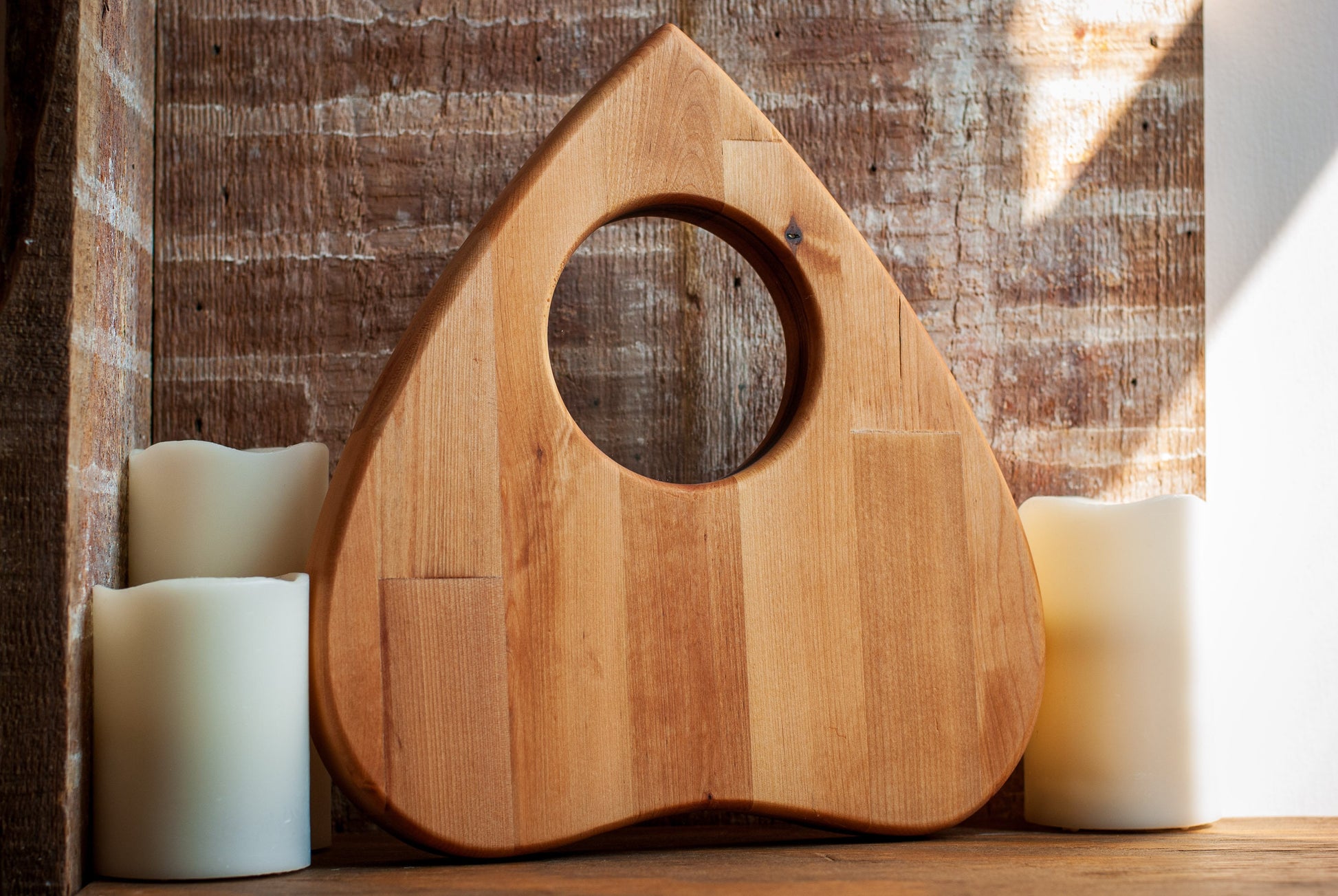 Wooden planchette-shaped cutting board with a circular hole on a wooden surface with candles