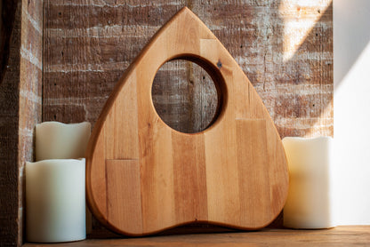 Wooden planchette-shaped cutting board with a circular hole on a wooden surface with candles