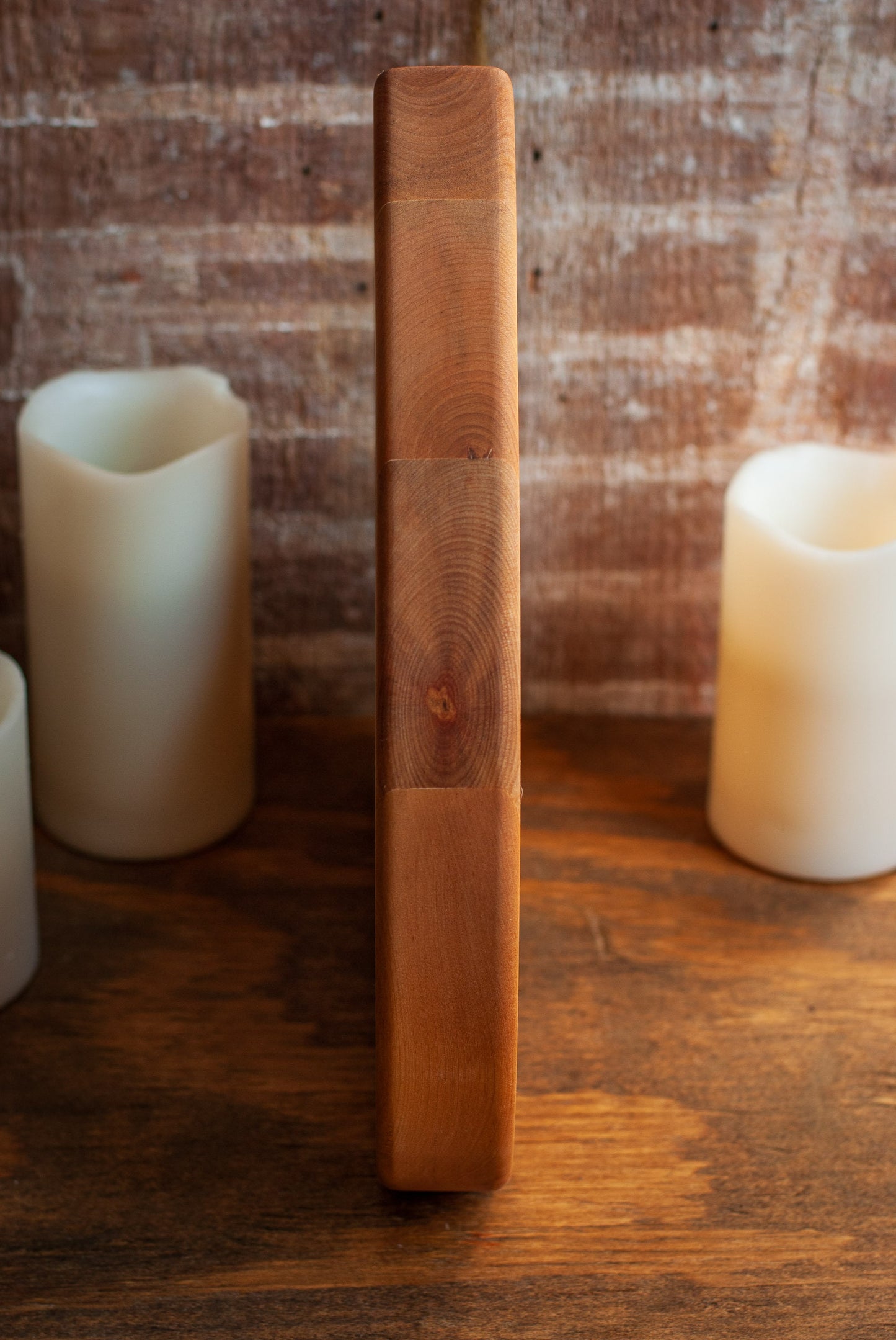 Side view of wooden planchette-shaped cutting board on a wooden surface with candles in the background