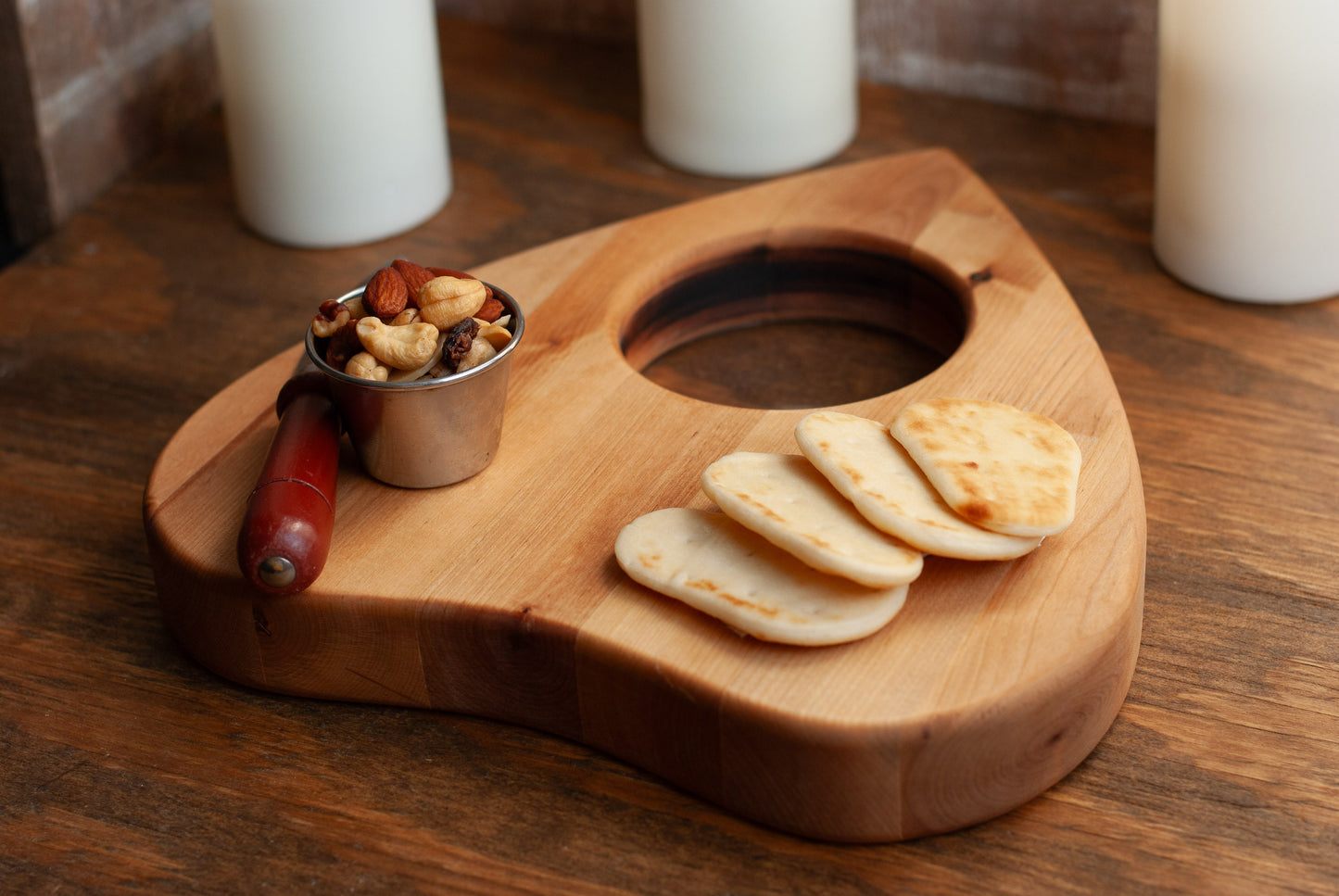 Wooden planchette-shaped charcuterie board with crackers, nuts, and a small bowl on a wooden surface.