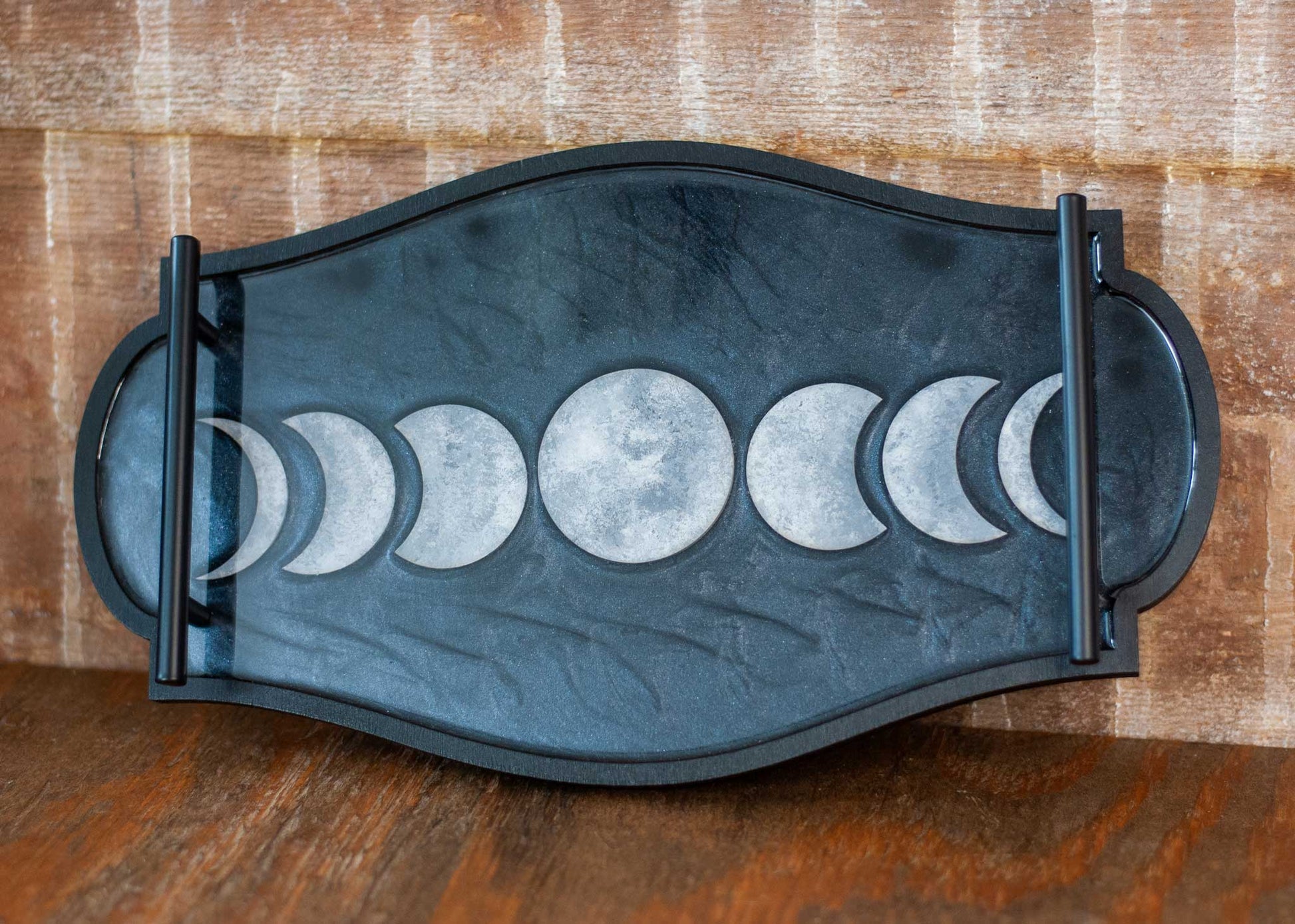 Decorative black and shimmery resin tray with moon phases on a wooden surface