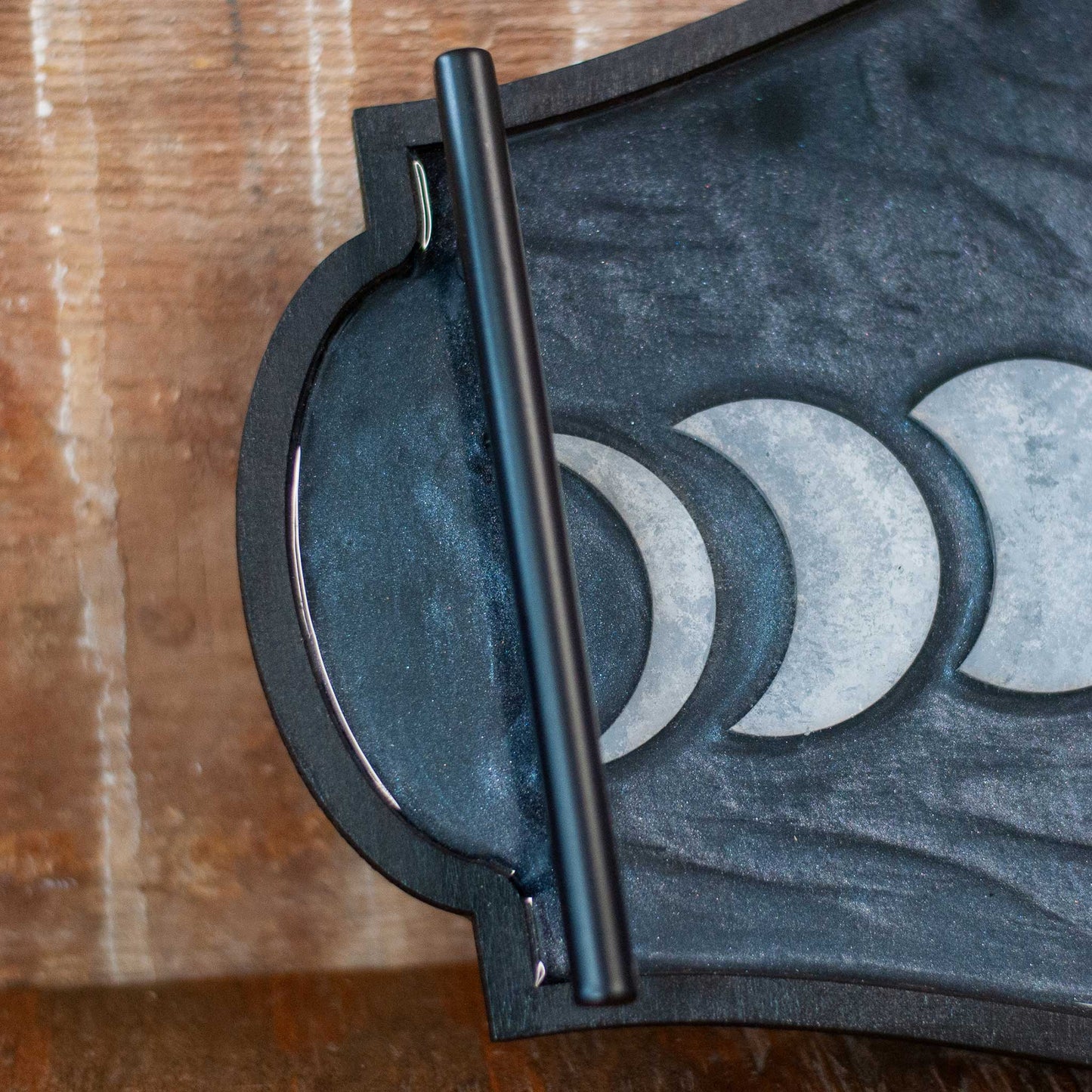 Decorative shimmery black wooden and resin tray with moon phases on a wooden surface
