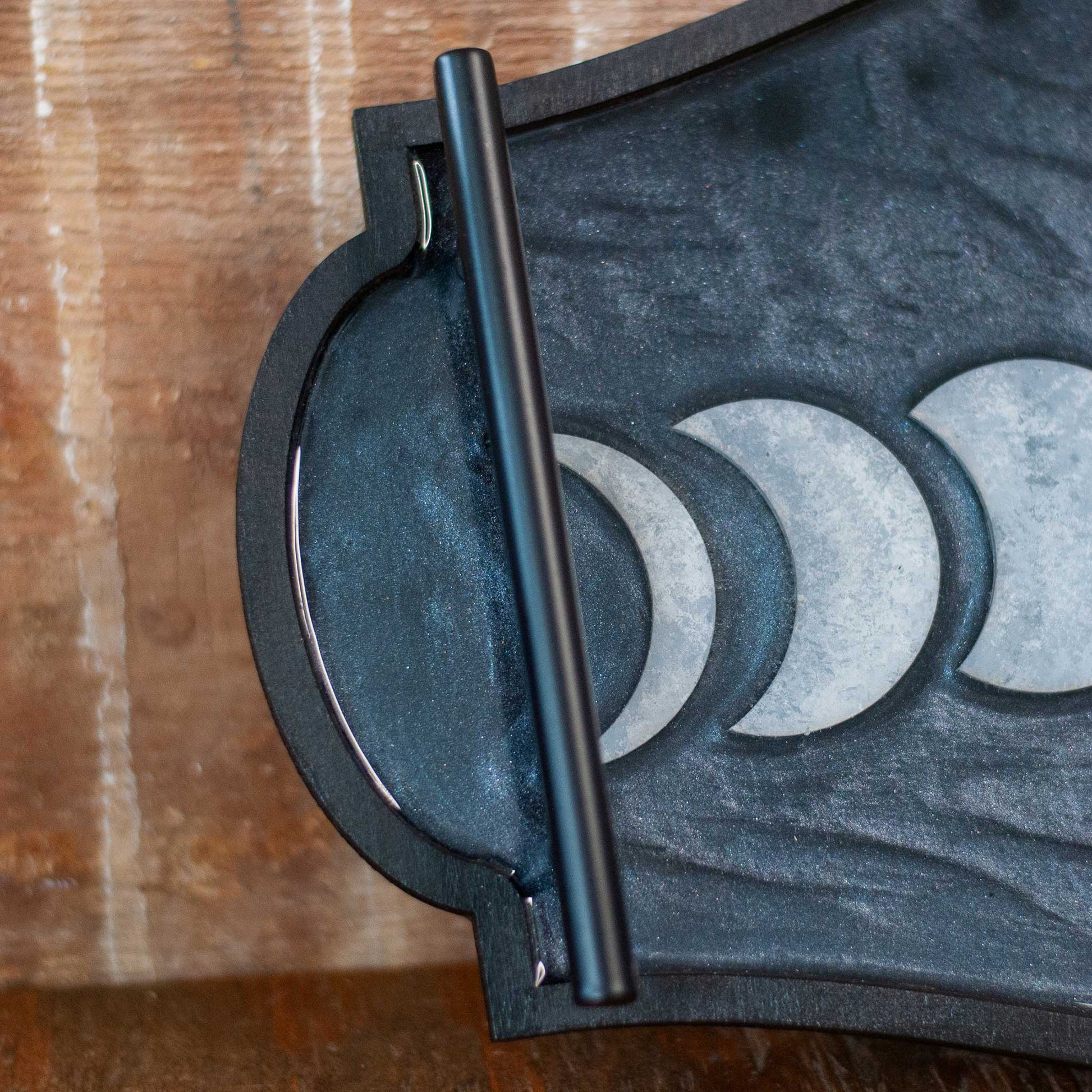Decorative shimmery black wooden and resin tray with moon phases on a wooden surface