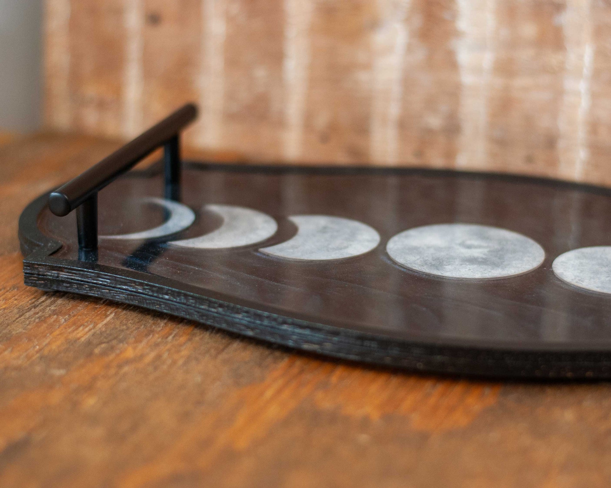 Decorative shimmery black wooden and resin tray with moon phases on a wooden surface