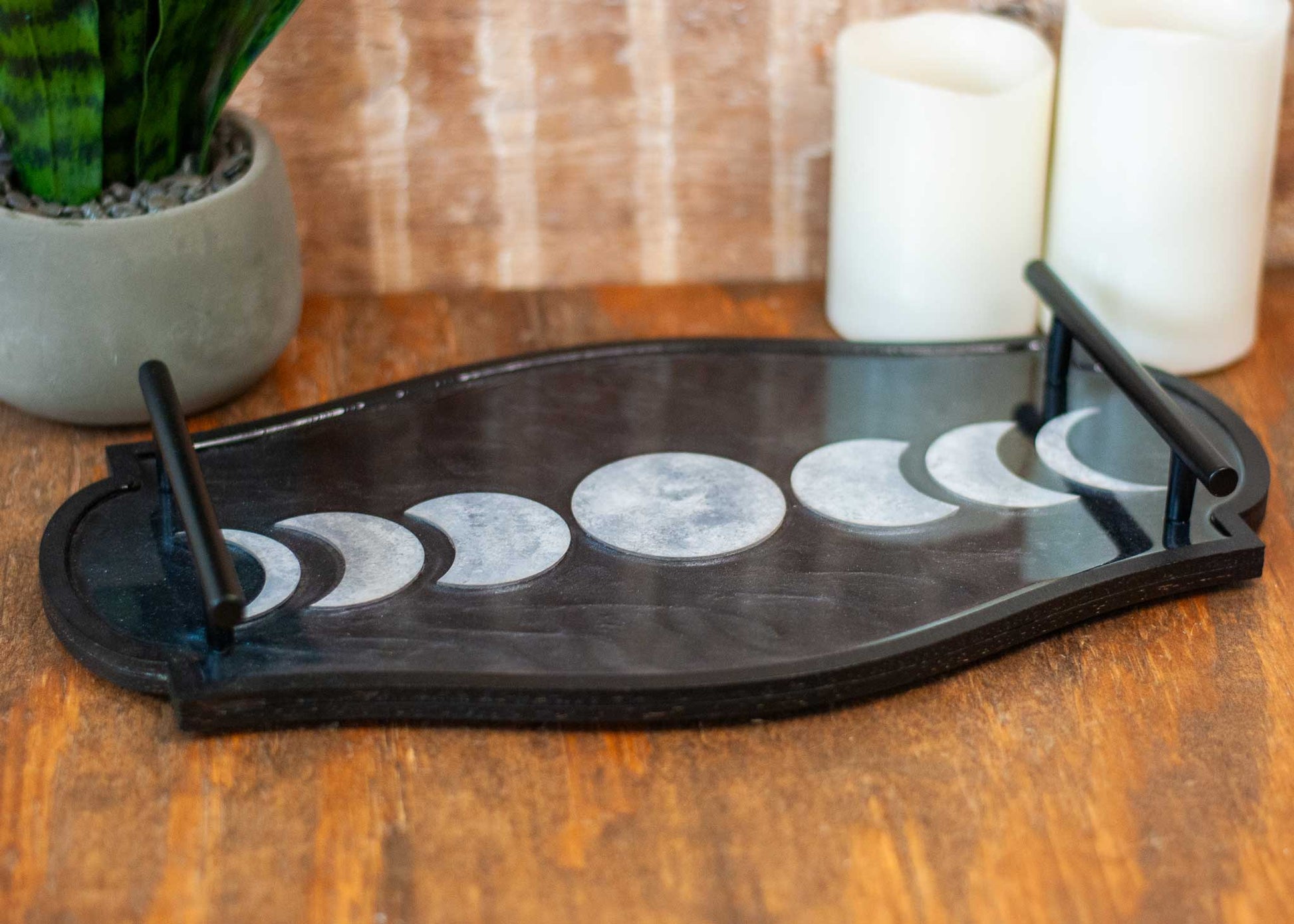 Decorative shimmery black wooden and resin tray with moon phases on a wooden surface with candles and plant